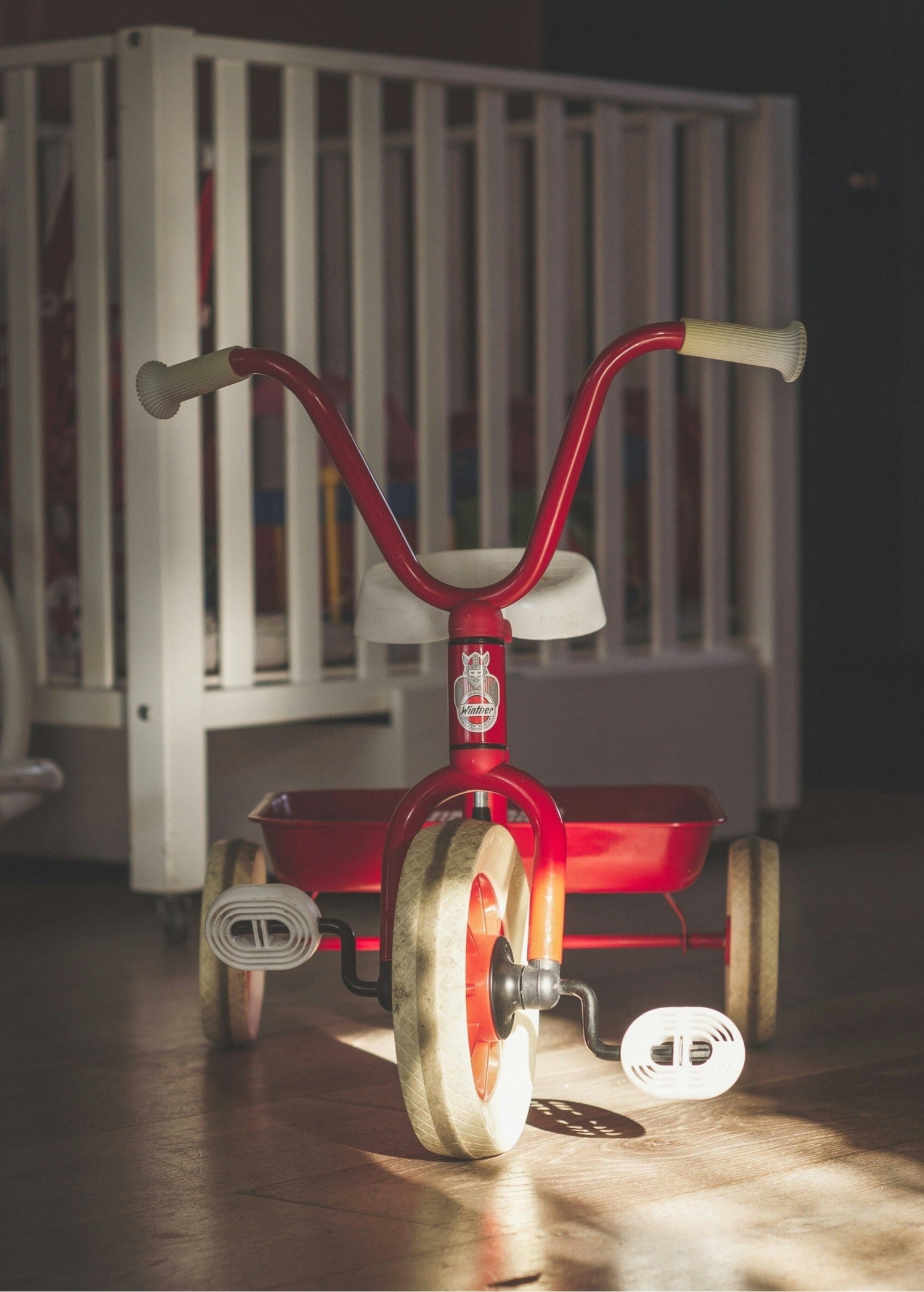 Red vintage bike for kids with high handle bar, white seat, grips and tires, in front of a white cot. NB Cycles